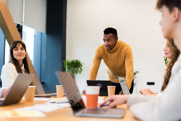 Black male team leader at business meeting in an office, discussing business affairs with other workers, papers with charts and gadgets on the table